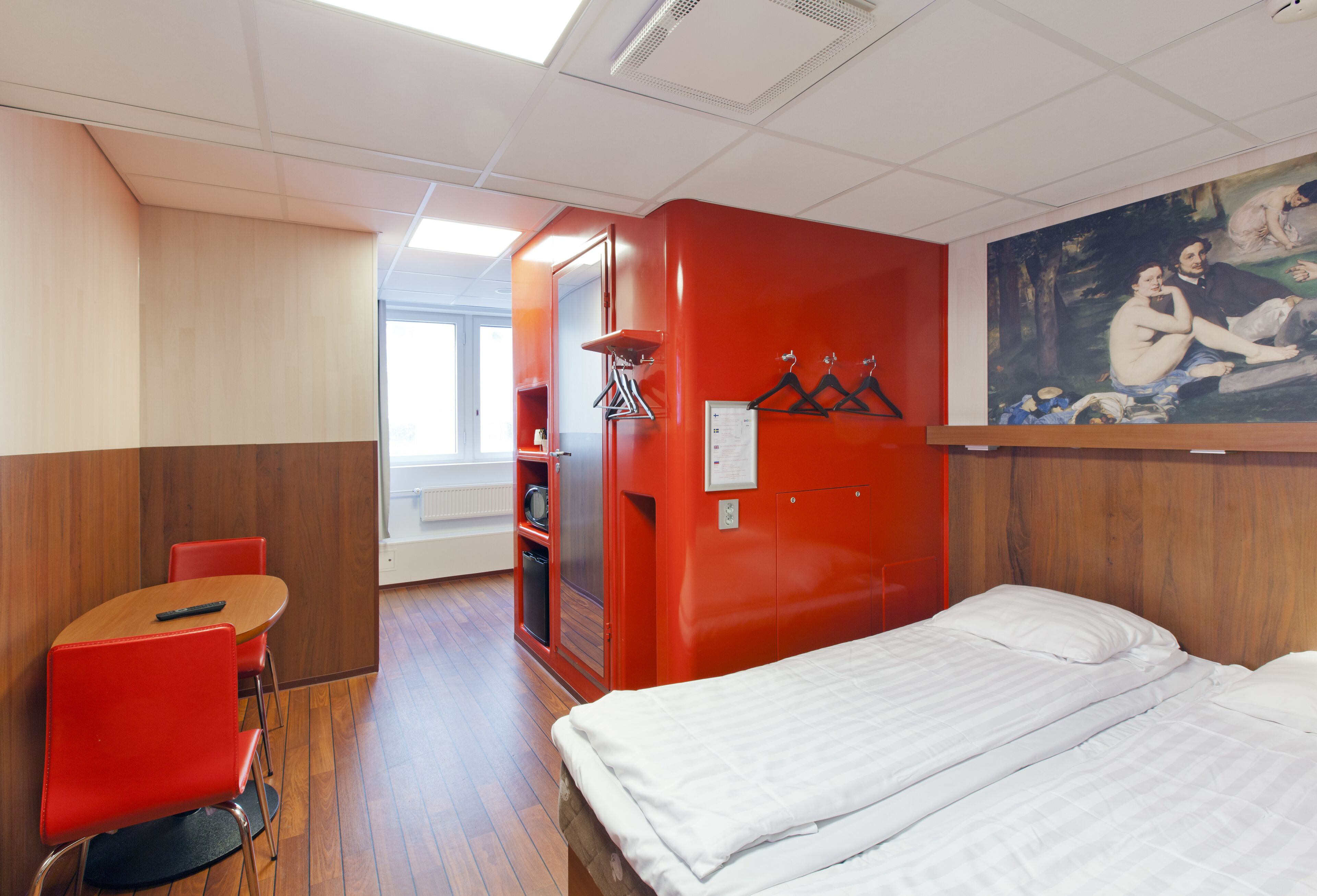 Une chambre d’hôtel avec un lit, un mur rouge, un tableau et une chaise rouge.