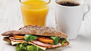 A sandwich with lettuce, tomato, and cheese, a glass of orange juice, and a cup of coffee on a white surface. - Omena Hotel Helsinki City Center (Helsinki)