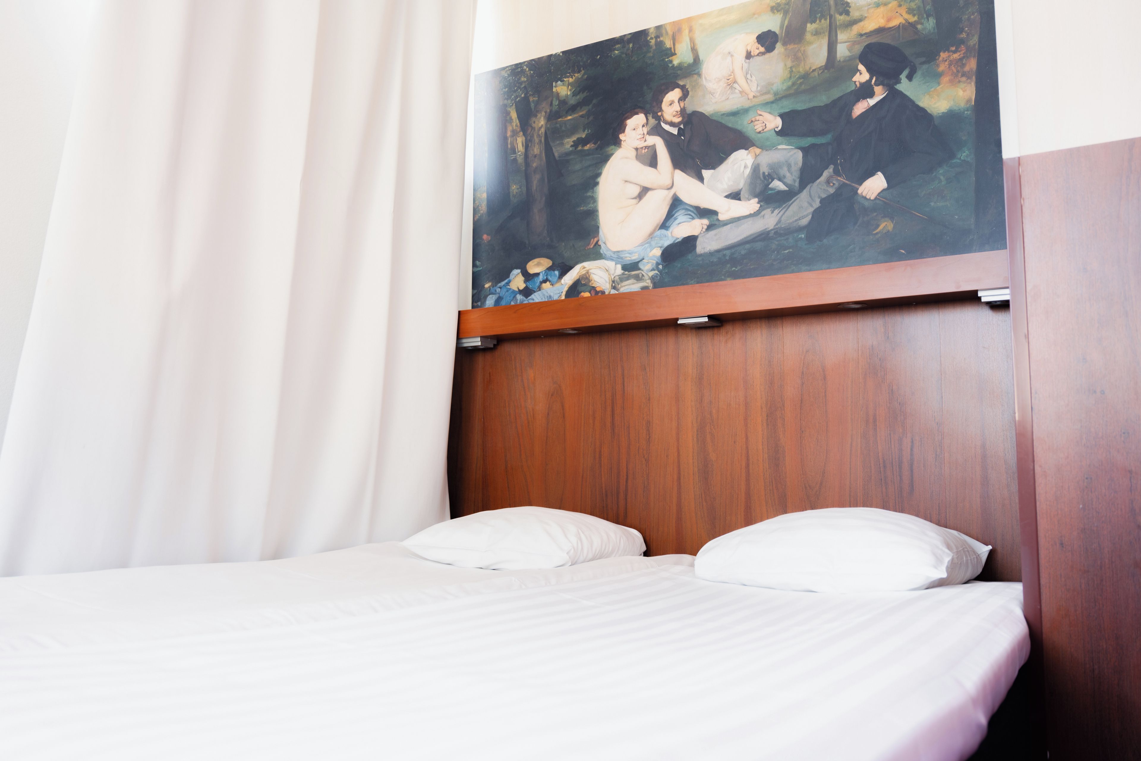 A hotel room with a wooden headboard, white bedding, and a painting of a historical scene above the bed.