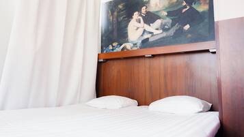 Habitación de hotel con cabecera de madera, ropa de cama blanca y un cuadro con una escena histórica sobre la cama.