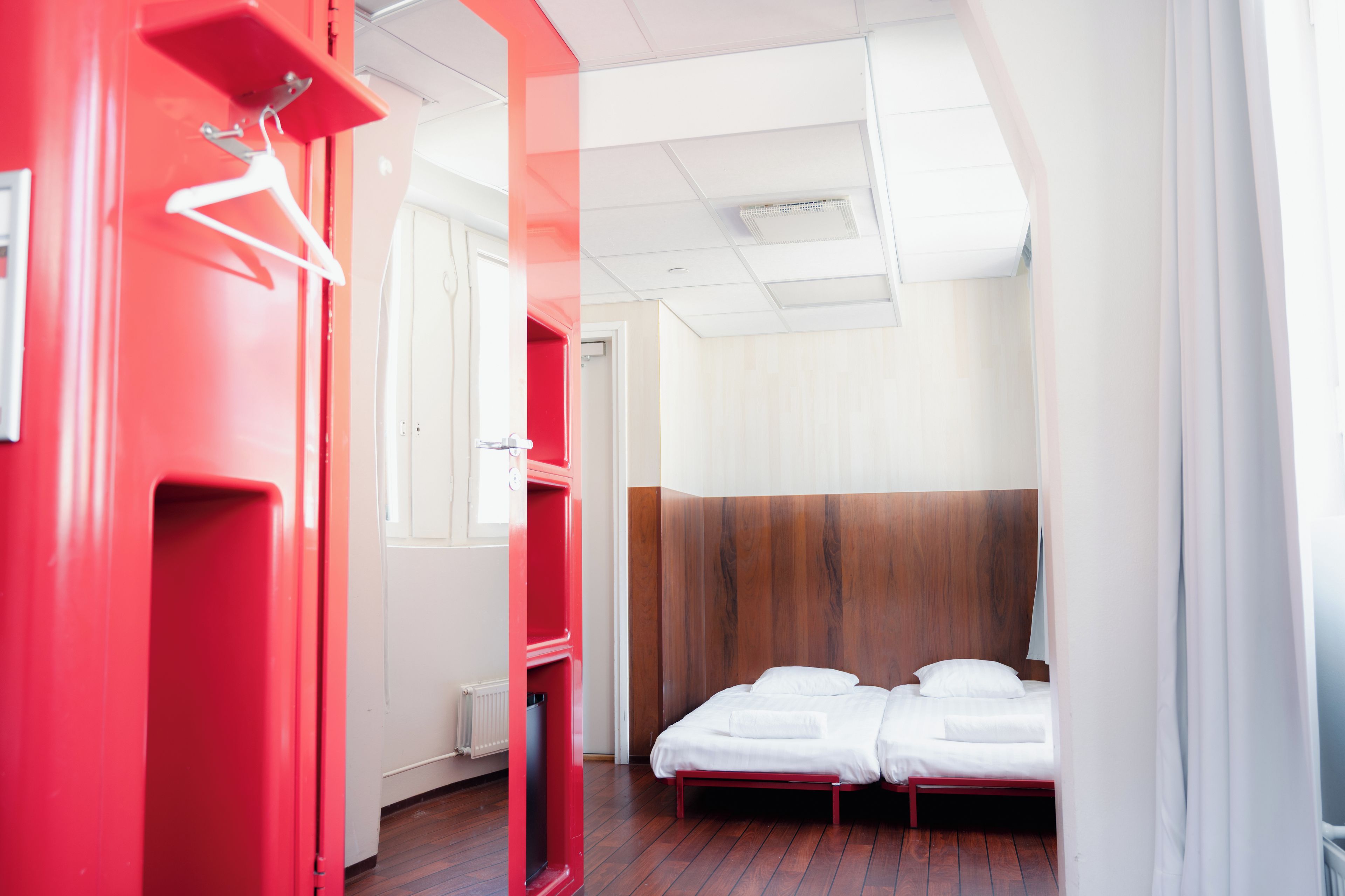A hotel room with a red wardrobe, a wooden headboard, and a bed with white bedding.