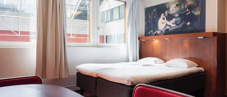 Una habitación de hotel con cama, un cuadro en la pared, una ventana con cortinas y una mesa con sillas.