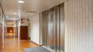 A hallway with wooden flooring, a gray mat at the entrance, and an elevator with a sign above it. - Omena Hotel Helsinki City Center (Helsinki)