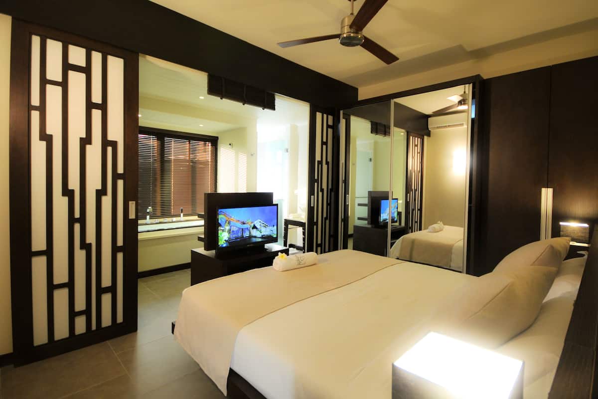 A hotel room with a large bed, a television, a desk, and a mirror.