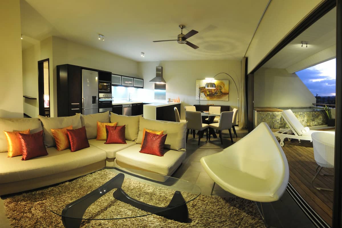 A modern living room with a sofa, a glass coffee table, and a dining area with a table and chairs.