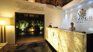 A reception area with a marble counter, a woman standing behind it, and a backdrop with the hotel name. - Domaine des Alizées by Fine and Country (Grand-Baie)