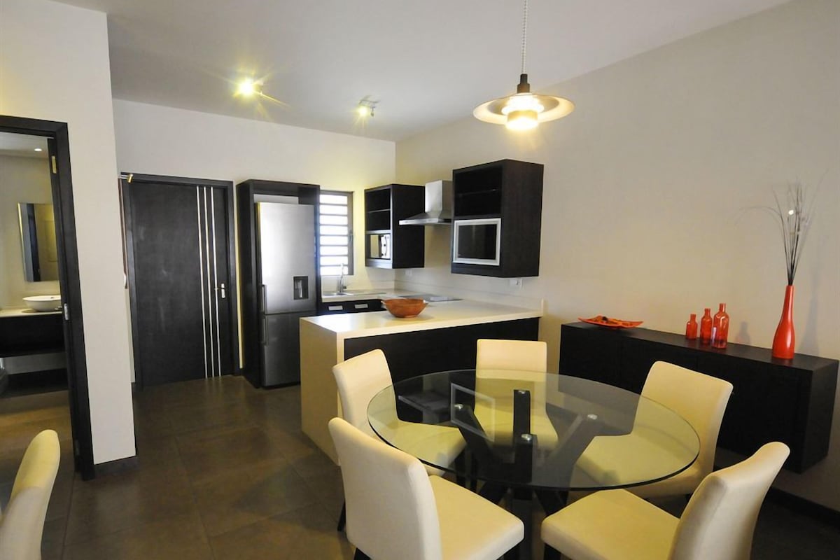 A modern kitchen with a central island, black cabinets, and a glass dining table with chairs.