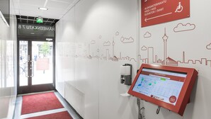 A hotel entrance with a digital information kiosk, a red carpet, and a cityscape mural on the wall. - Omena Hotel Tampere (Tampere)