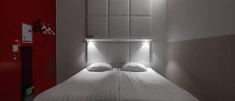 Une chambre d’hôtel avec un lit, une tête de lit dotée d’un panneau lumineux, un mur rouge et un petit placard.