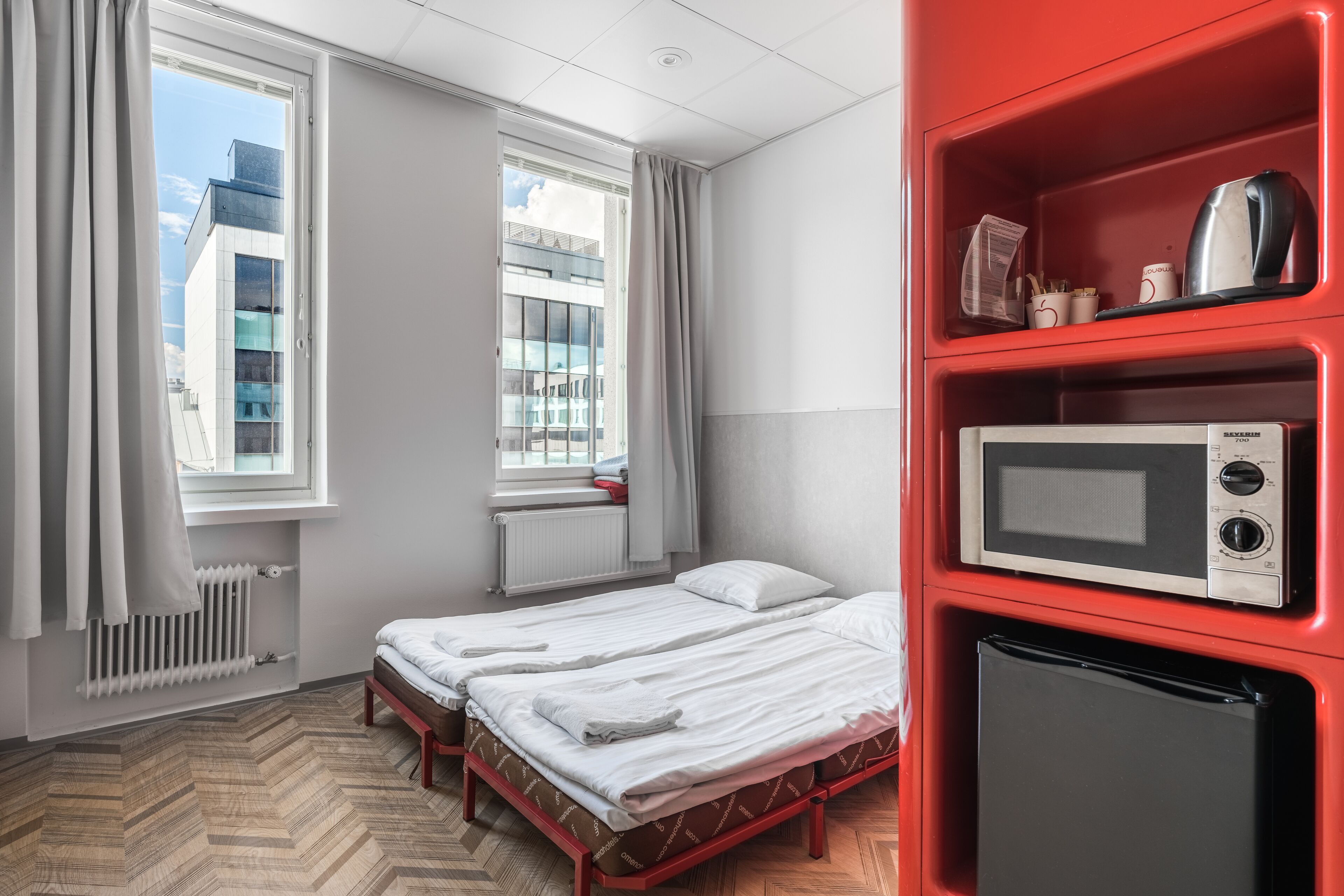 A hotel room with two beds, a red minibar, a microwave, and a window with curtains.