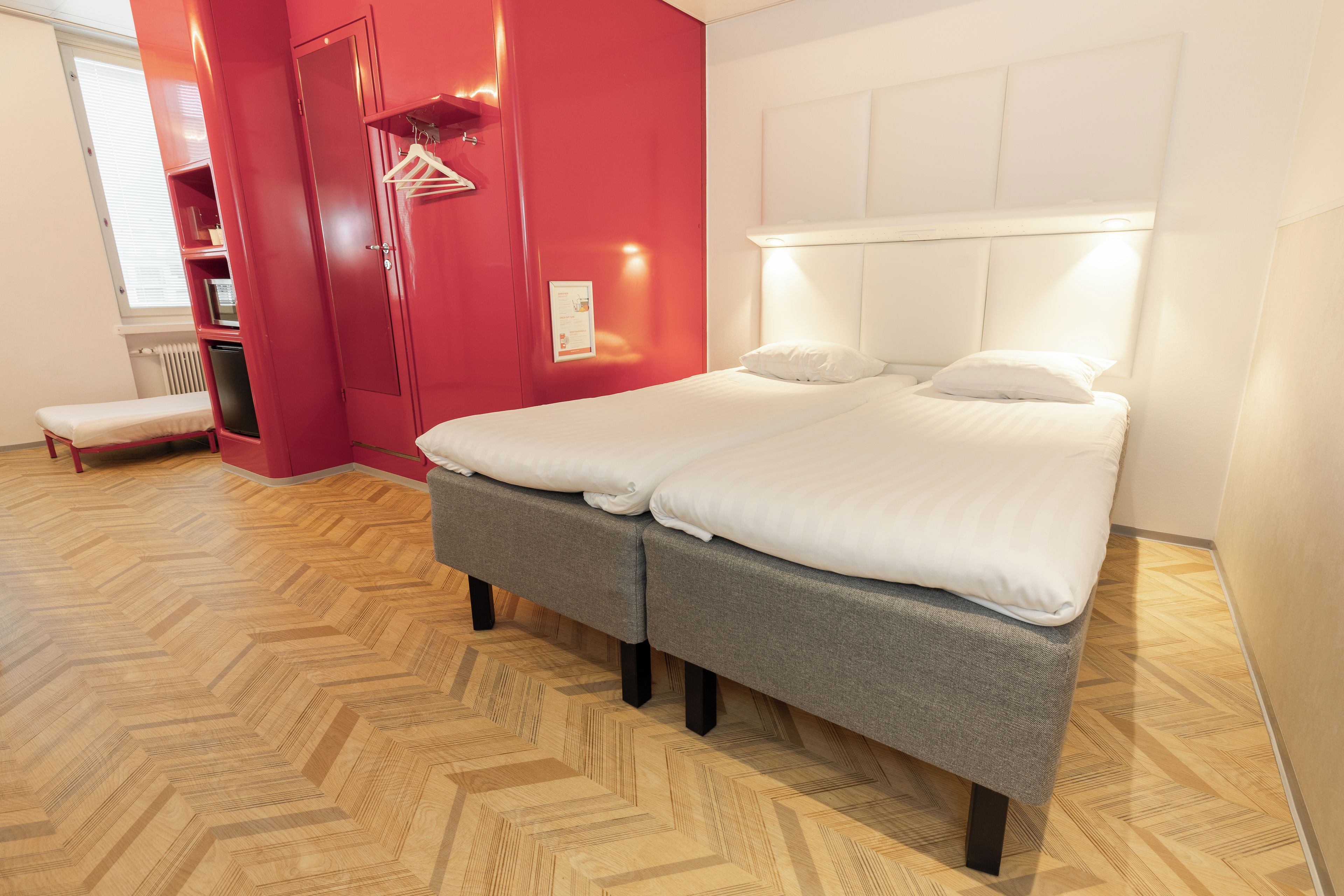 Une chambre d’hôtel avec un lit, un banc, un mur rouge et une tête de lit blanche.