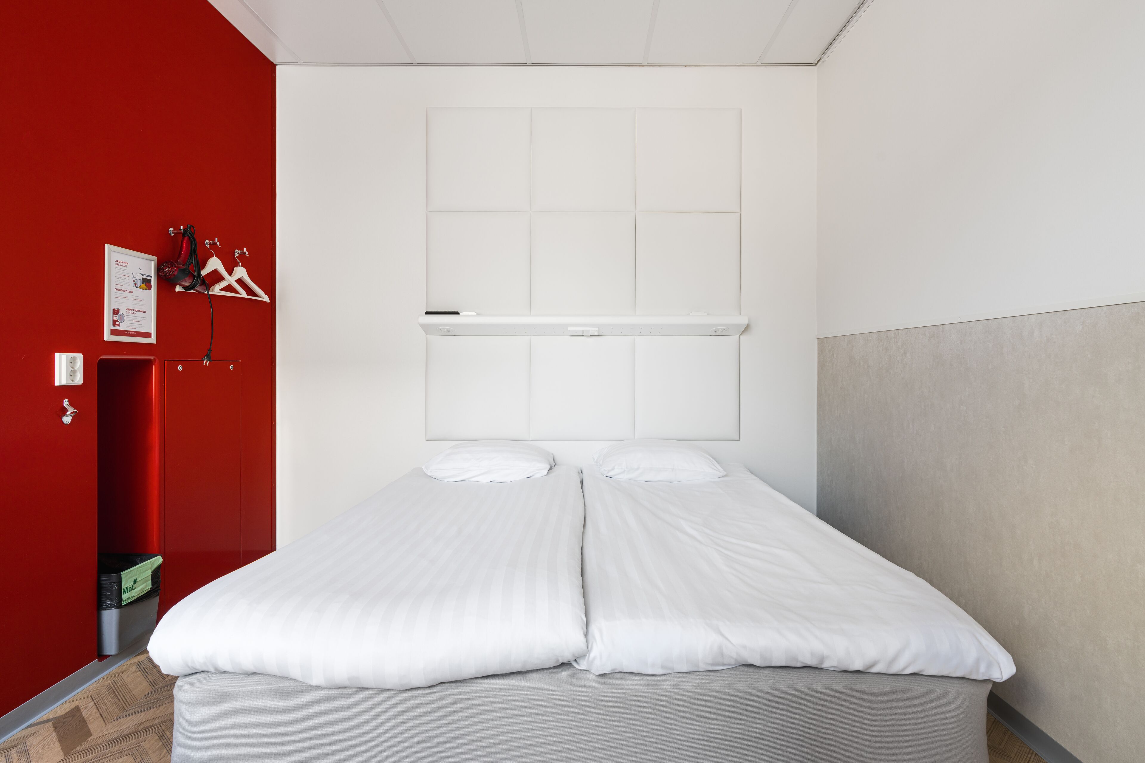 A double bed with white linens, a white headboard, and a red accent wall.