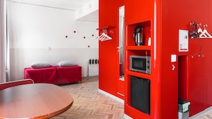 A room with a red wall, a wooden table, a red sofa, a microwave, a small refrigerator, and a heater. - Omena Hotel Tampere (Tampere)