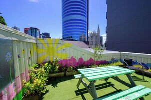 Un giardino pensile con un tavolo da picnic verde, murales colorati e uno skyline sullo sfondo.