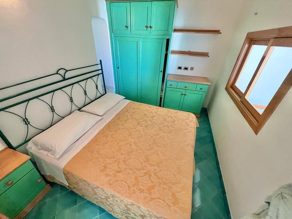 Une chambre à coucher avec un lit, une armoire verte, une petite table et une fenêtre.