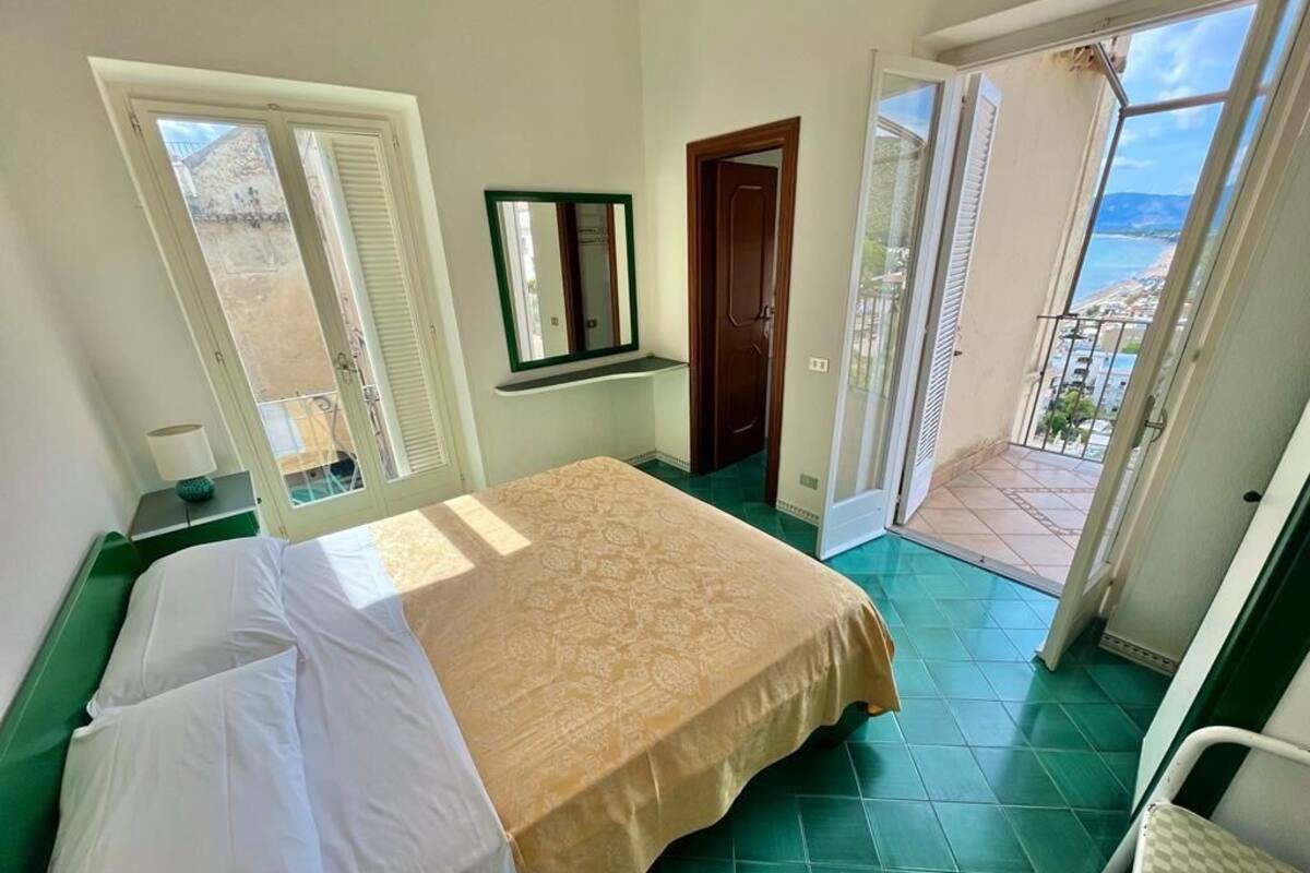 Ein Schlafzimmer mit Bett, Fenster, Tür und Blick ins Freie.