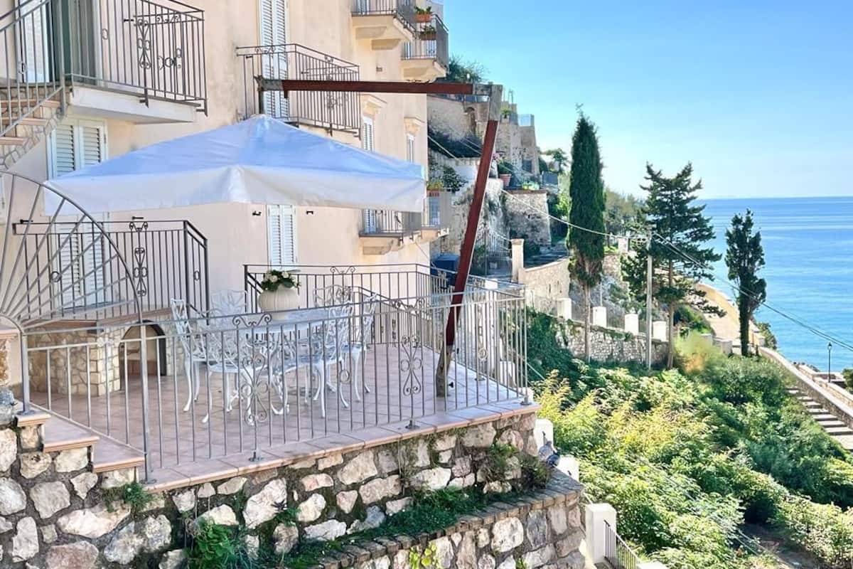 Ein Balkon mit Gartenmöbeln, einer Steinmauer und Blick aufs Meer.