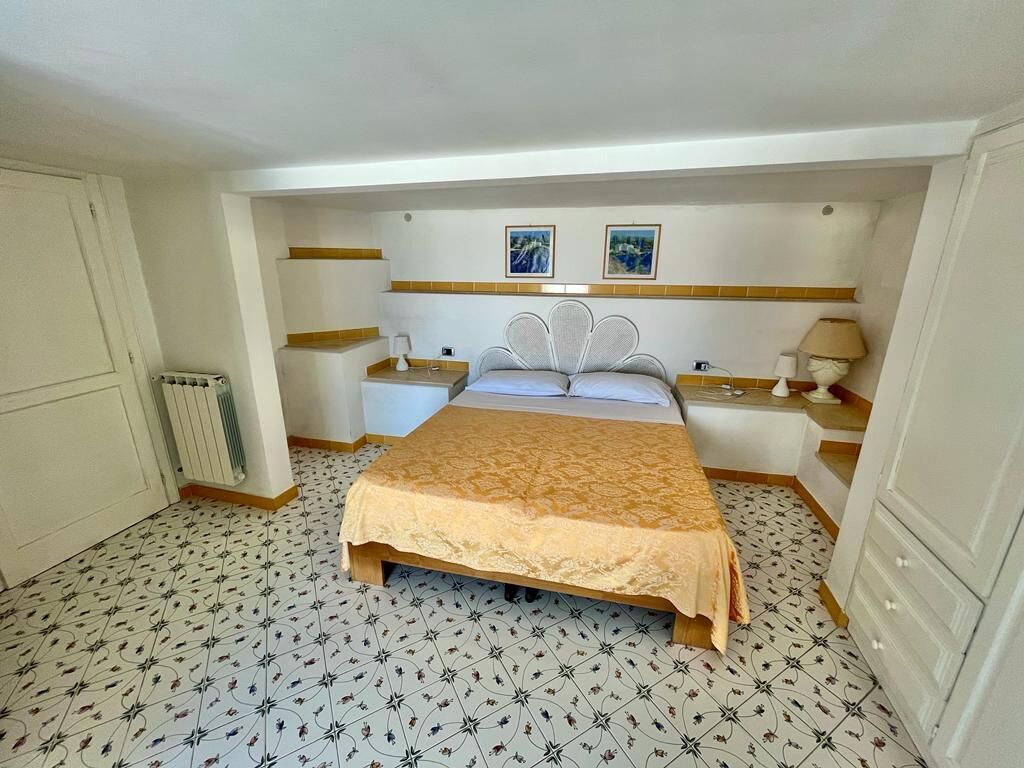 Um quarto com cama, mesas de cabeceira, um radiador e duas imagens emolduradas na parede.