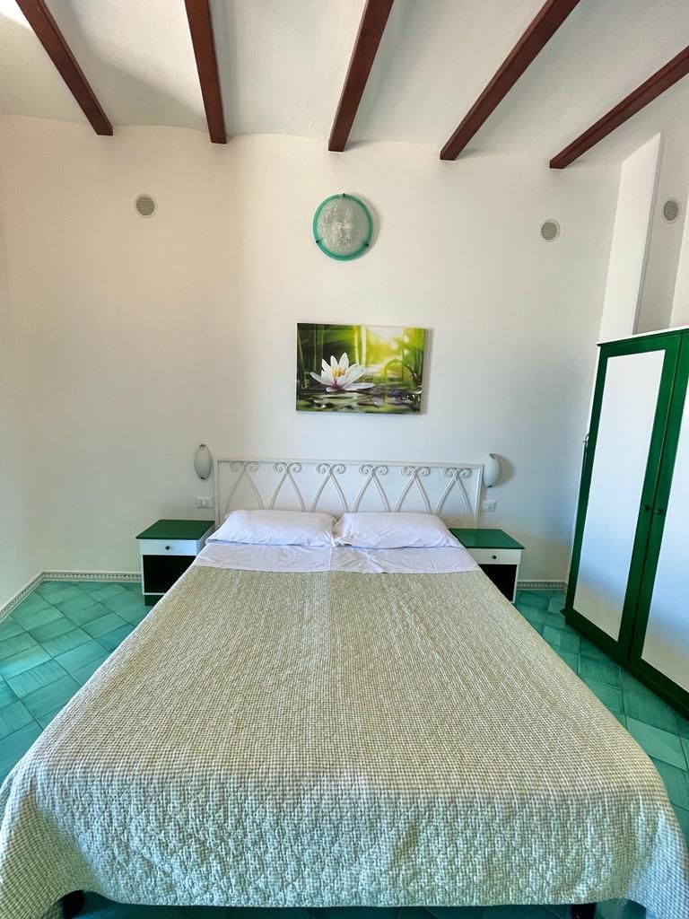 Una camera da letto con un letto, un comodino, un'armadio verde, una sveglia a muro e un quadro di un fiore di loto.