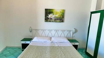 Una camera da letto con un letto, un comodino, un'armadio verde, una sveglia a muro e un quadro di un fiore di loto.
