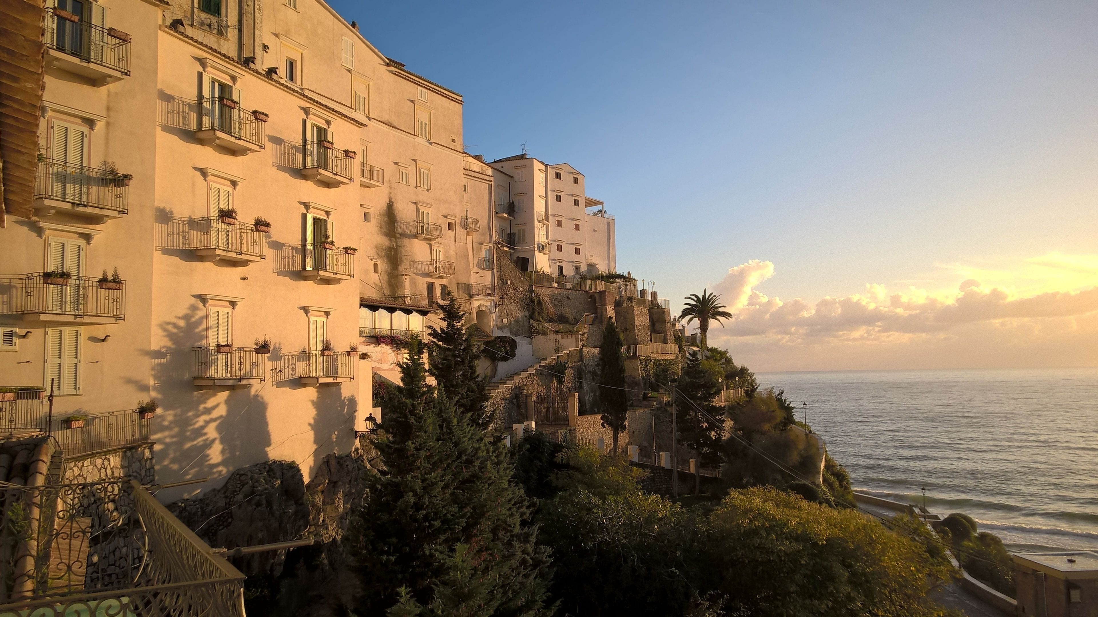 A coastal building with balconies, a staircase, and a view of the sea.