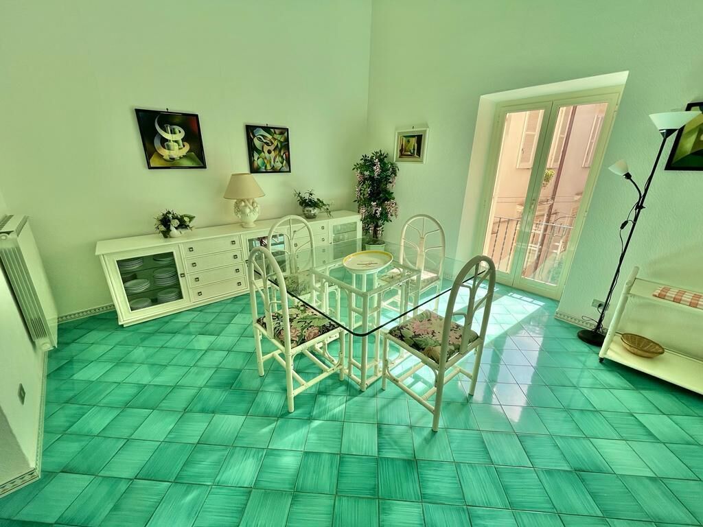 A room with a green-tiled floor, a white dining table with chairs, a white cabinet, and a window with a view.