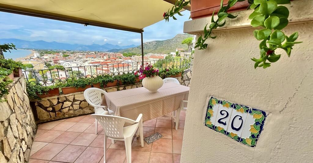 A balcony with a table and chairs, a potted plant, and a number plaque.