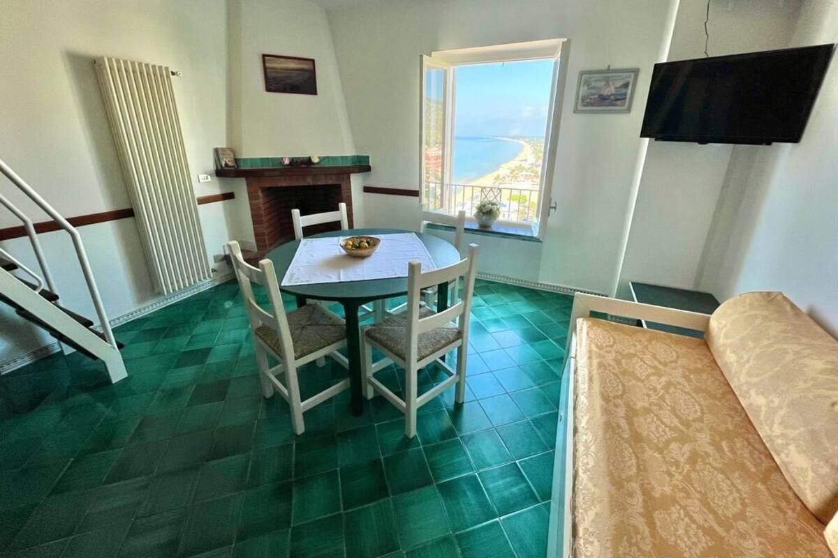 Ein Zimmer mit Esstisch und Stühlen, einem Kamin, einem an der Wand befestigten Fernseher und einem Fenster mit Meerblick.