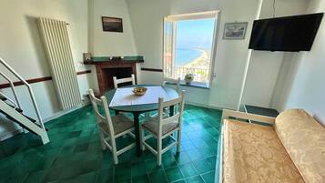 Una stanza con un tavolo da pranzo e sedie, un camino, una TV fissata al muro e una finestra vista mare.