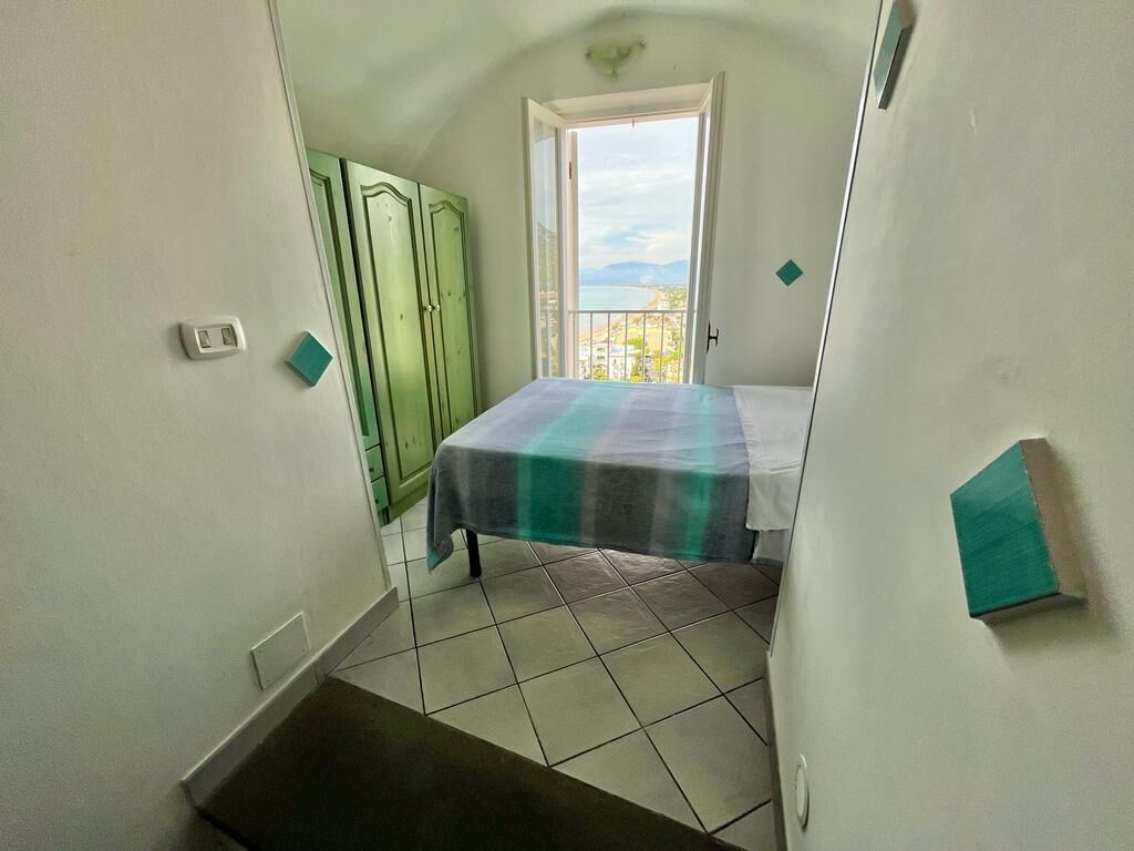 A narrow room with a bed, a green wardrobe, and a window with a view.