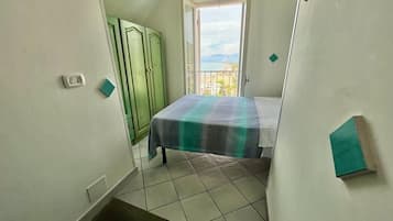 A narrow room with a bed, a green wardrobe, and a window with a view.