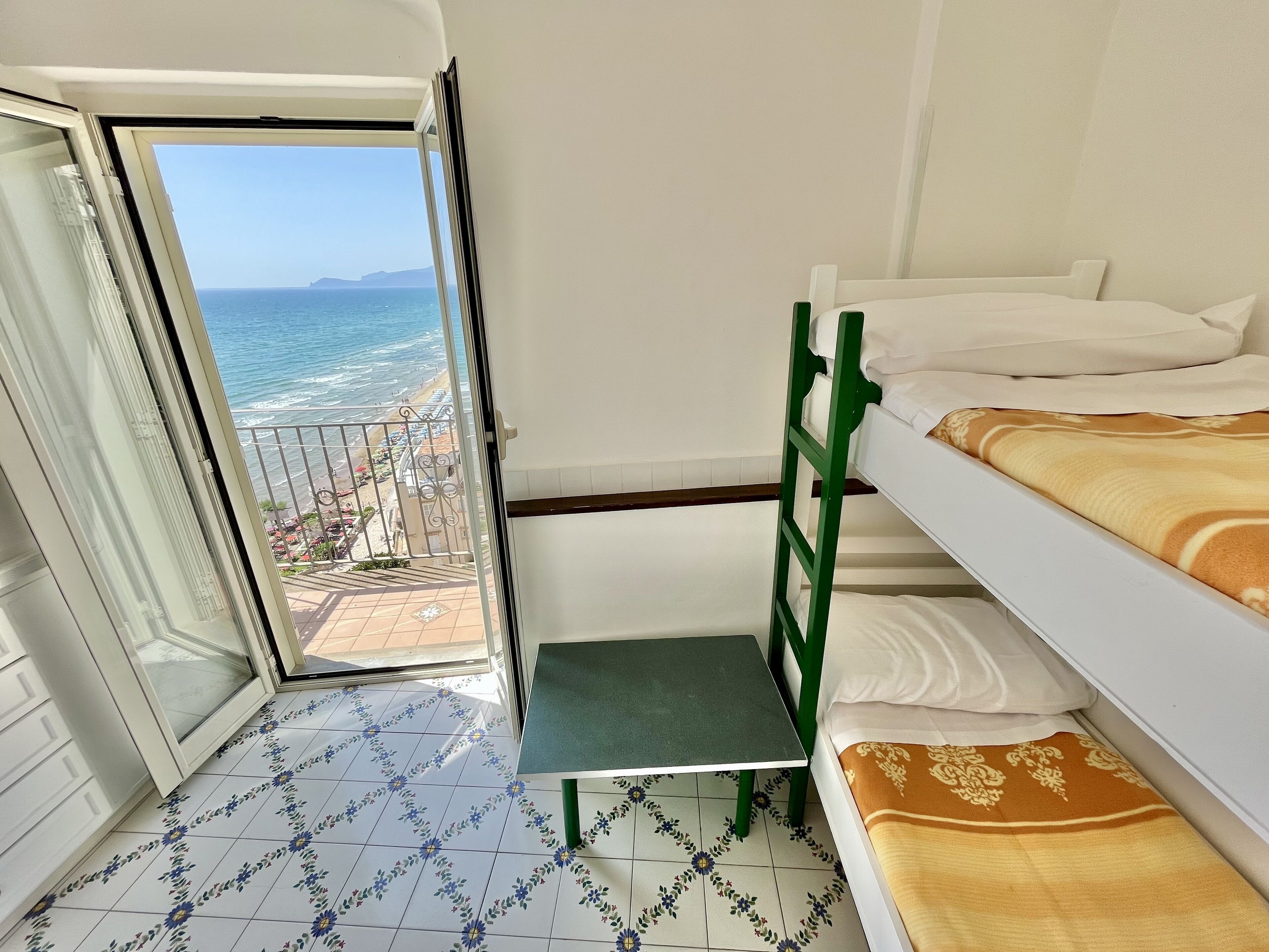 Ein Zimmer mit einem Etagenbett, einem kleinen Tisch und Blick auf das Meer durch eine geöffnete Tür.