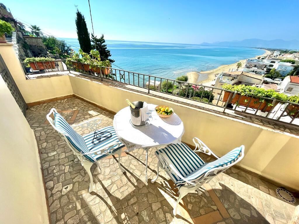 Un balcón con dos sillas a rayas y una mesa, con vista a la playa y al océano.