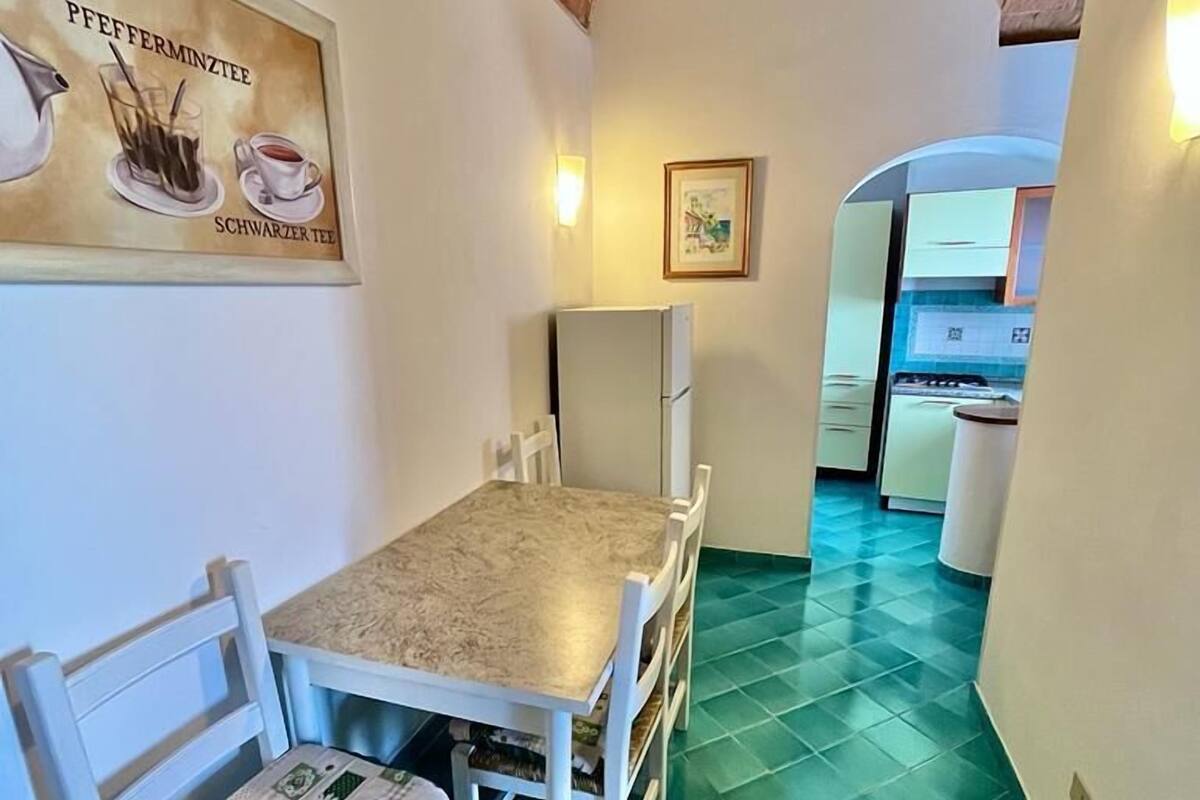 Ein Essbereich mit Tisch und Stühlen, im Hintergrund eine Küche und ein Fliesenboden.