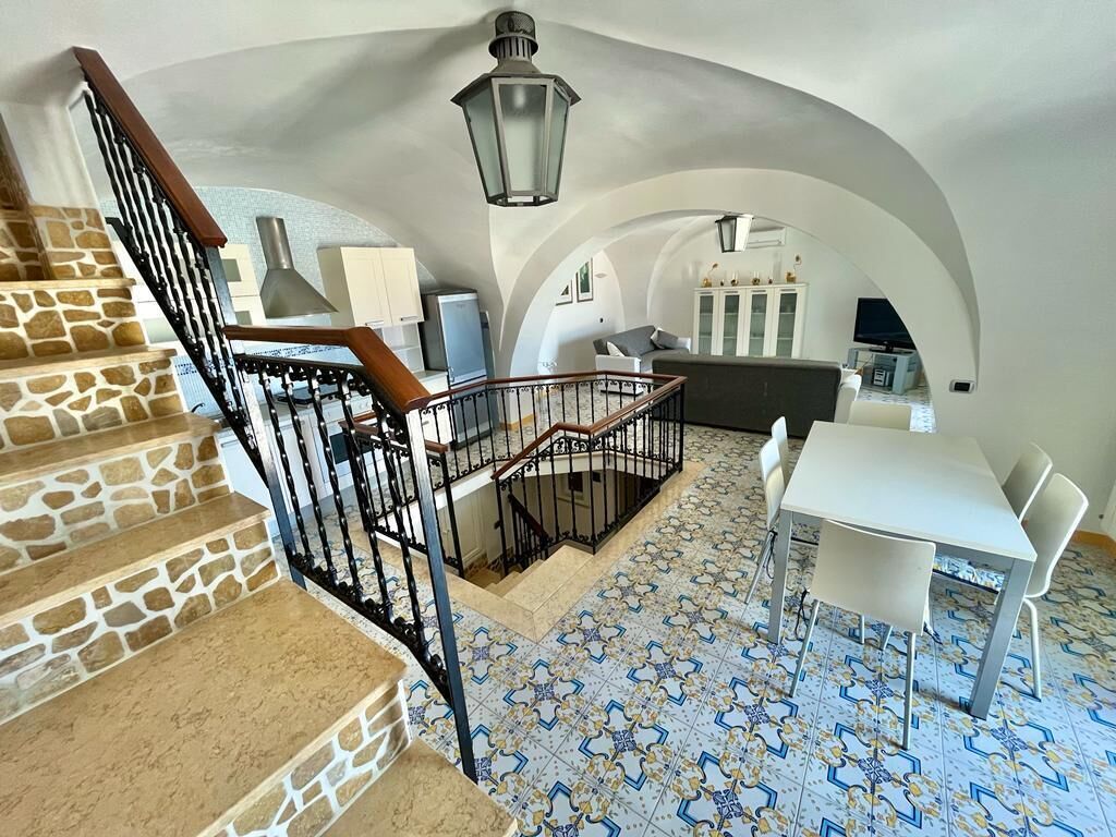 Amplia sala de estar con escalera, una mesa de comedor con sillas y una cocina visible a través de un arco.