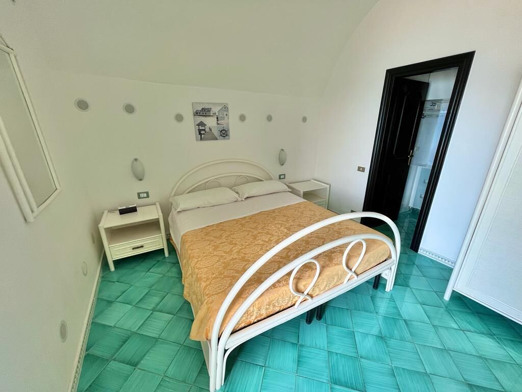 A bedroom with a bed, a nightstand, a wall-mounted light, and a door.