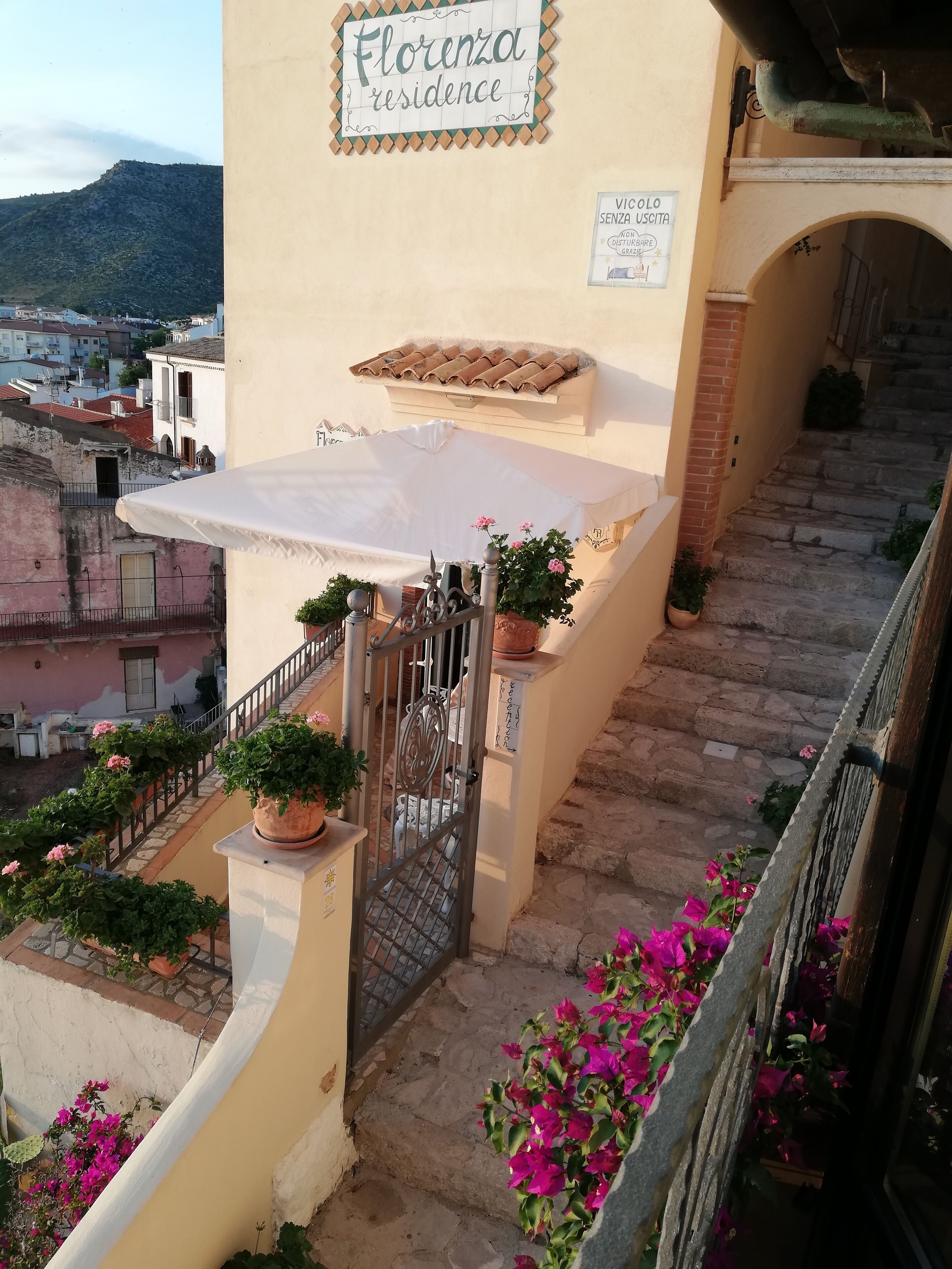A residential building named "Florenza residence" with a staircase leading to a covered area with potted plants and flowers.