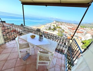 Un balcón con mesa y sillas, con vistas a un pueblo costero y al mar.