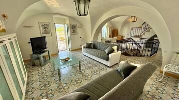 A spacious living room with a high arched ceiling, a sofa, a television, and a glass coffee table.