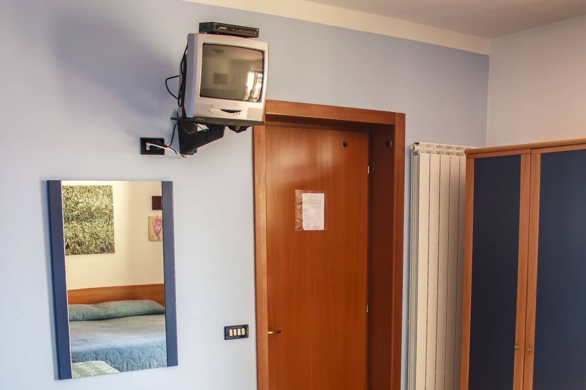 A room with a bed, a mirror, a television mounted on the wall, and a wardrobe.