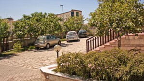 Une rue résidentielle bordée de voitures garées, avec un chemin de pierre et un escalier menant à un immeuble.