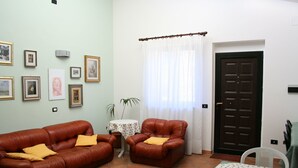 Un salon avec un canapé en cuir marron, un fauteuil en cuir marron, une petite table recouverte d’une nappe à pois et une porte en bois foncé.