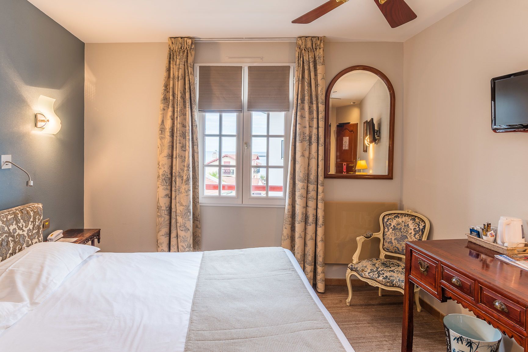 Ein Hotelzimmer mit einem Bett, einem Schreibtisch, einem Stuhl, einem Spiegel und einem fenster mit Vorhängen.