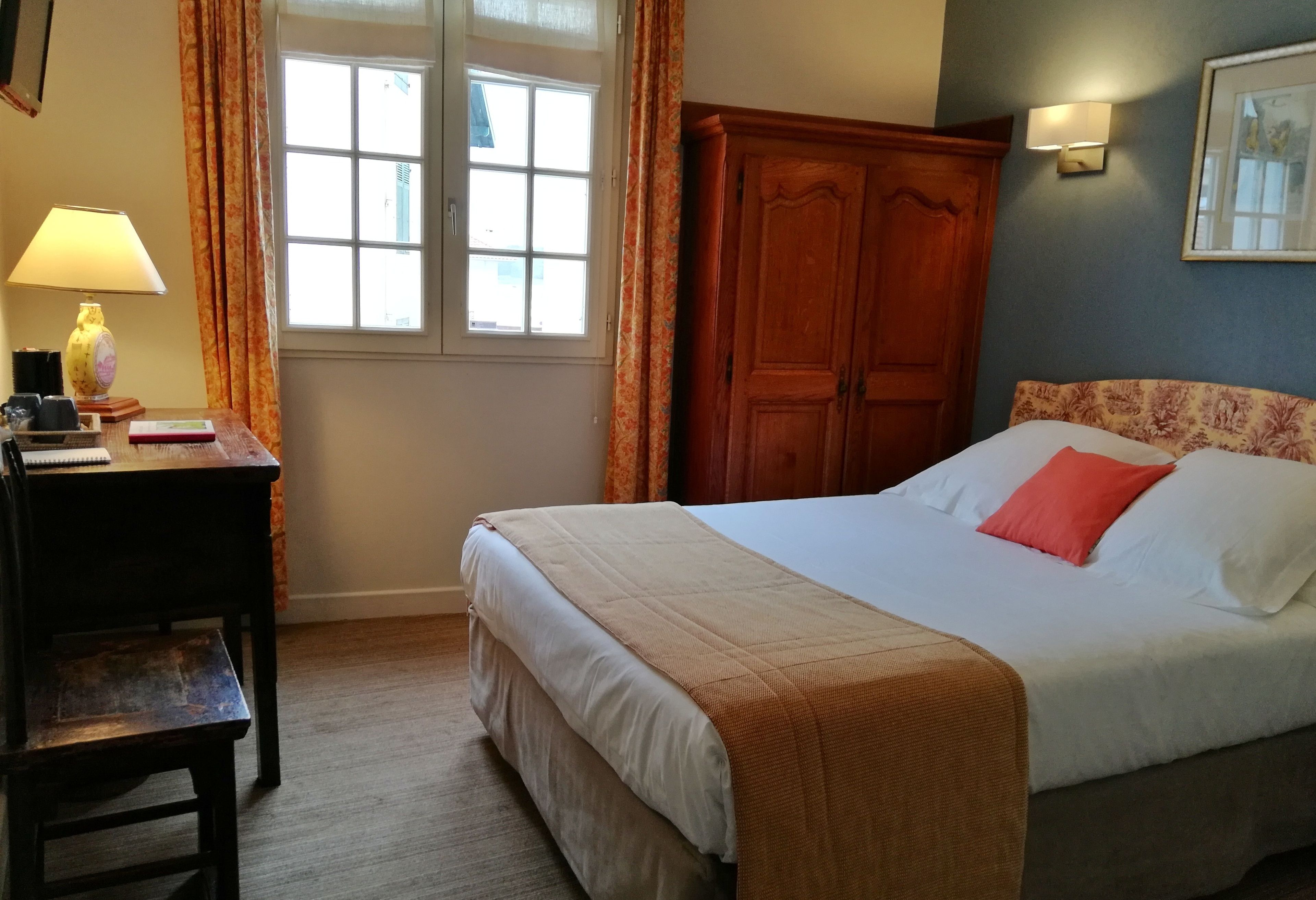 A hotel room with a bed, a desk with a lamp, a wardrobe, and a window with curtains.