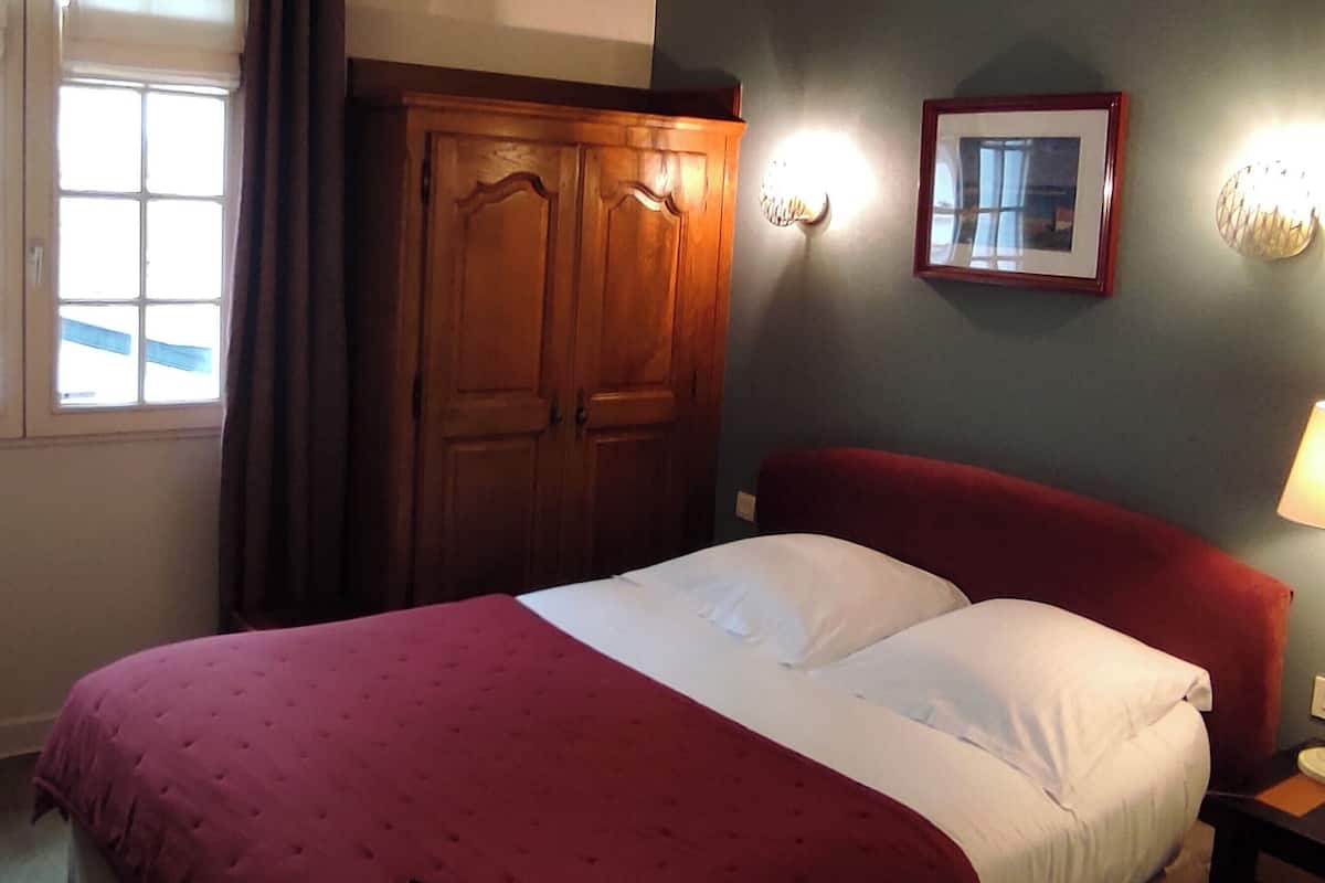 Een hotelkamer met een bed, een houten garderobe, een wandlamp en een ingelijste foto.