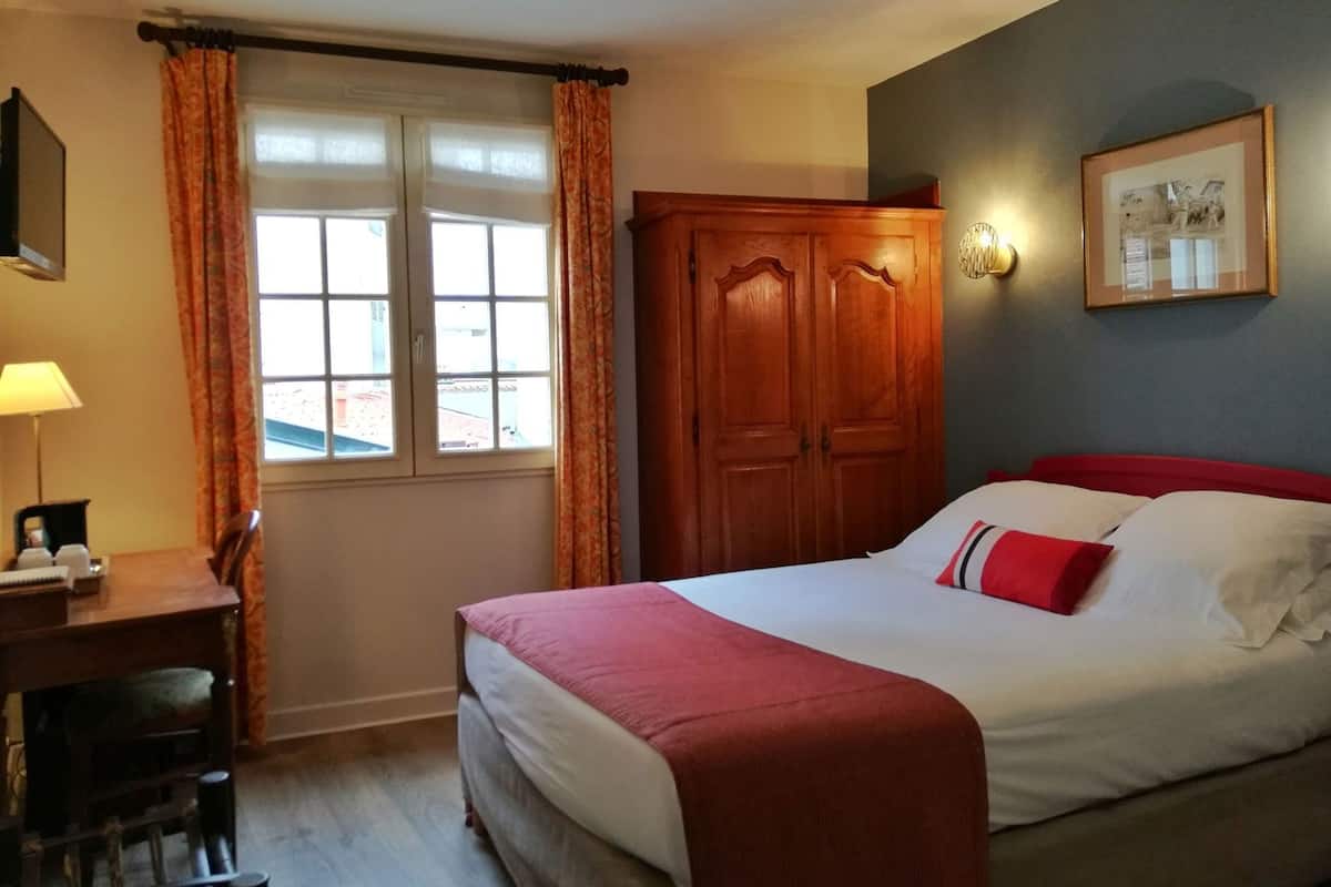 Een hotelkamer met een bed, een bureau, een stoel, een kledingkast en een raam met gordijnen.