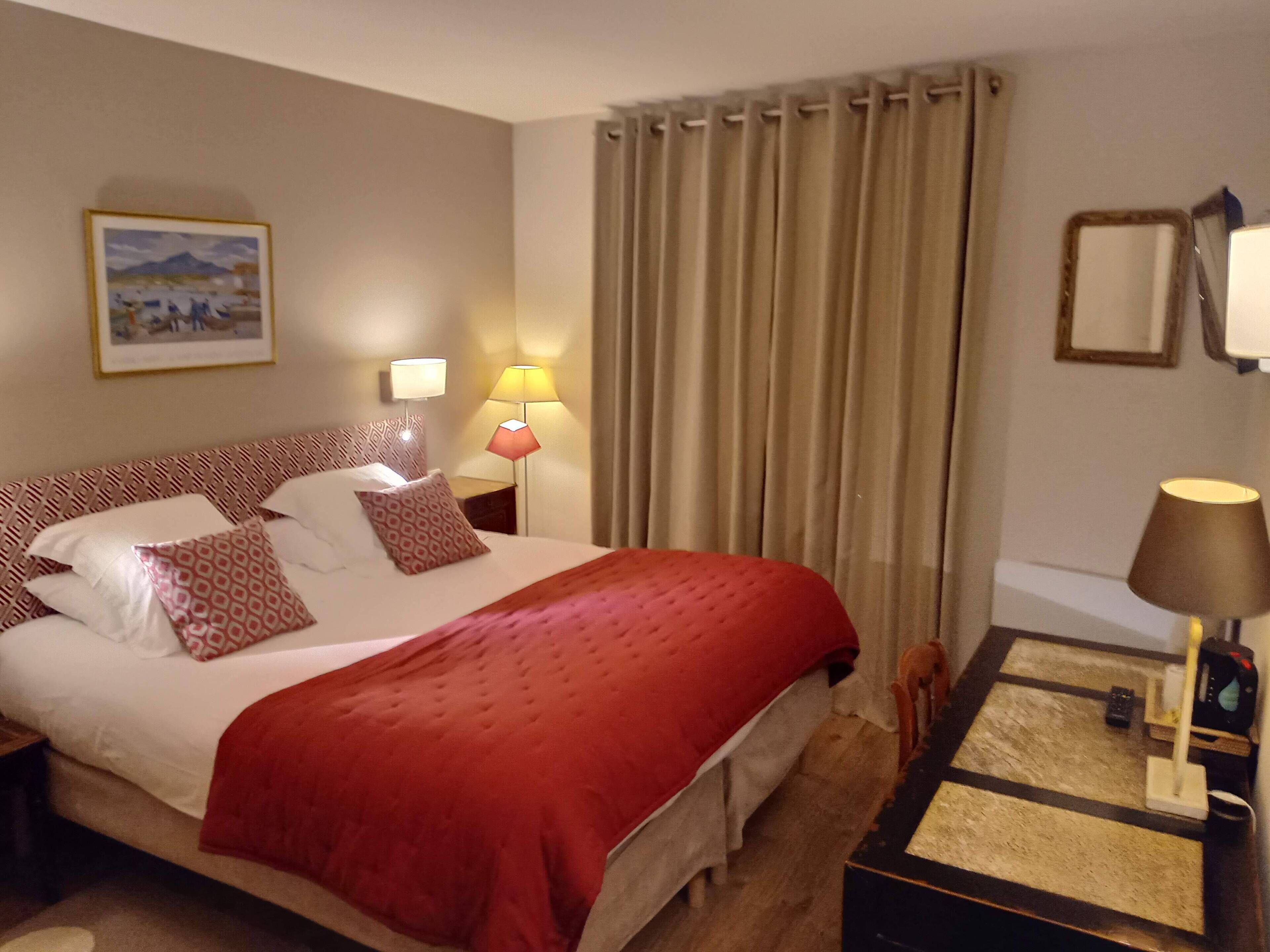 Une chambre d’hôtel avec un grand lit, deux lampes de chevet, une table de nuit, un miroir et un tableau au mur.