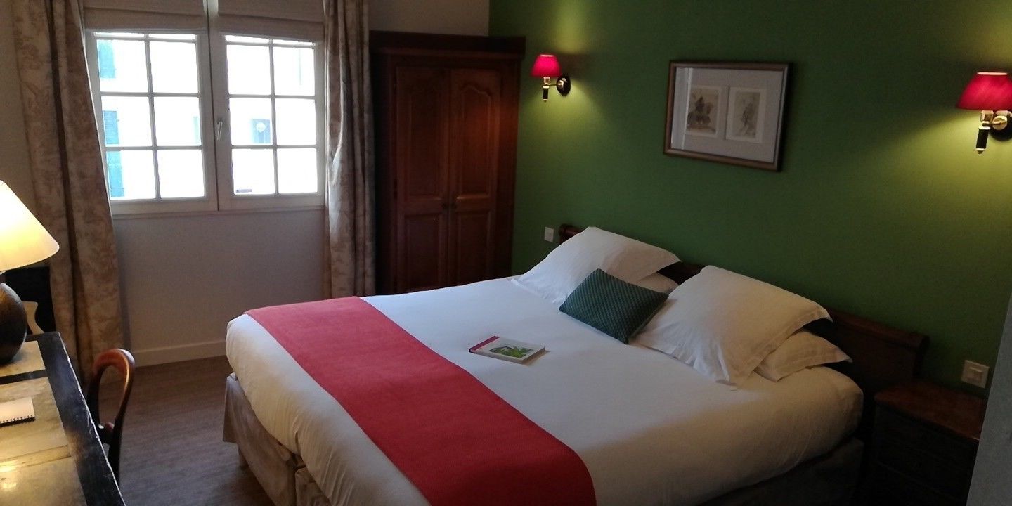 Una cama bien hecha con una colcha rojo y blanco, dos lámparas de noche y un cuadro en la pared.