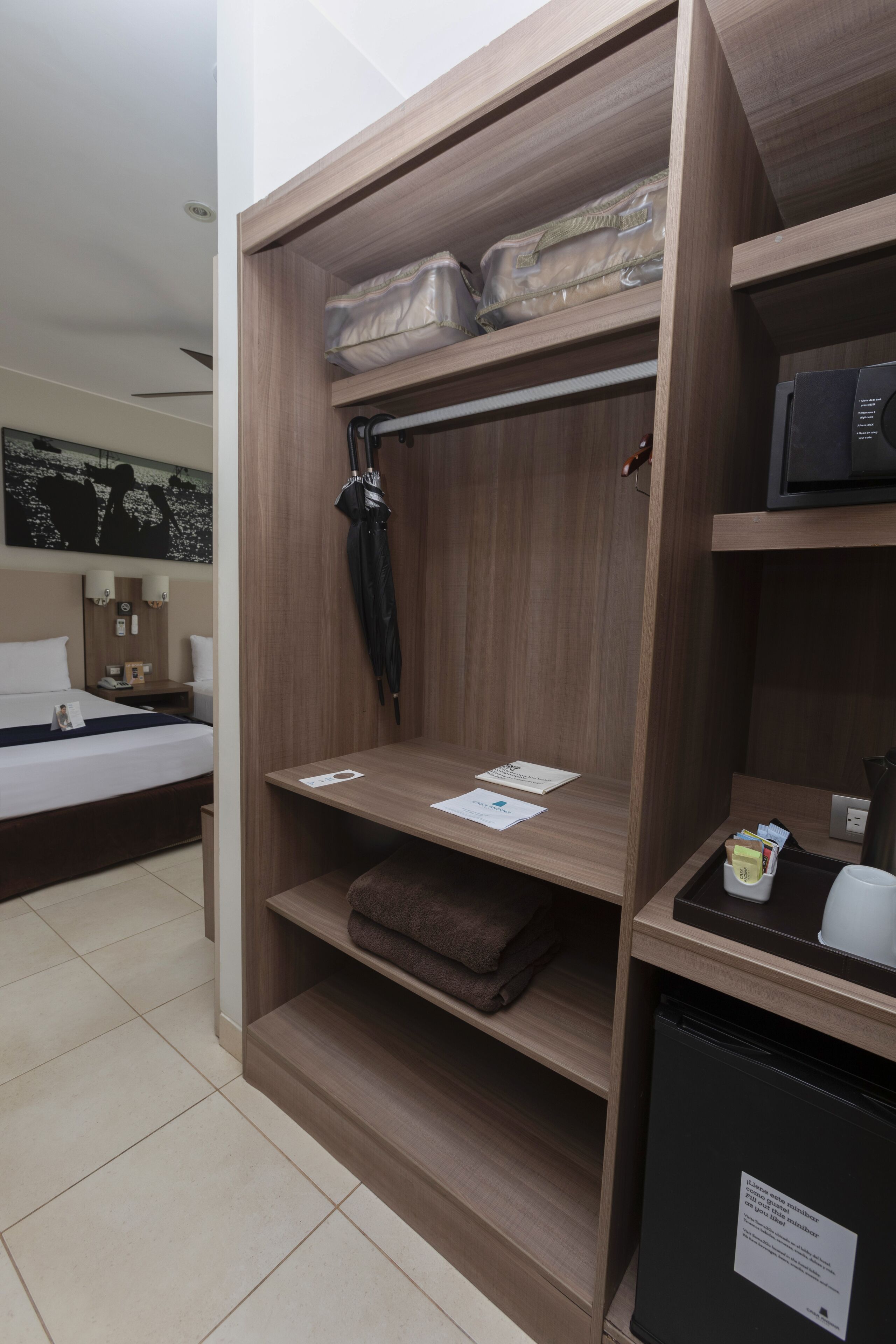 Habitación de hotel con armario de madera, cama, escritorio con computadora y refrigerador pequeño.