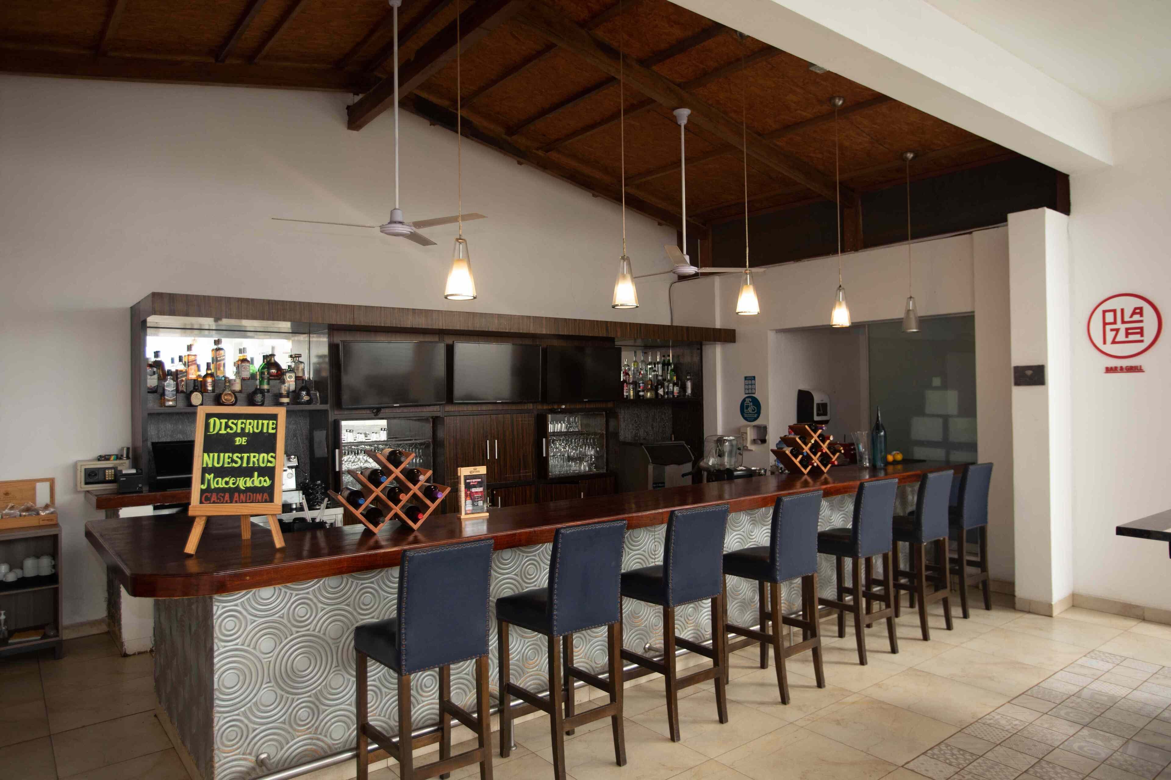 A bar area with a wooden counter, bar stools, and hanging pendant lights.